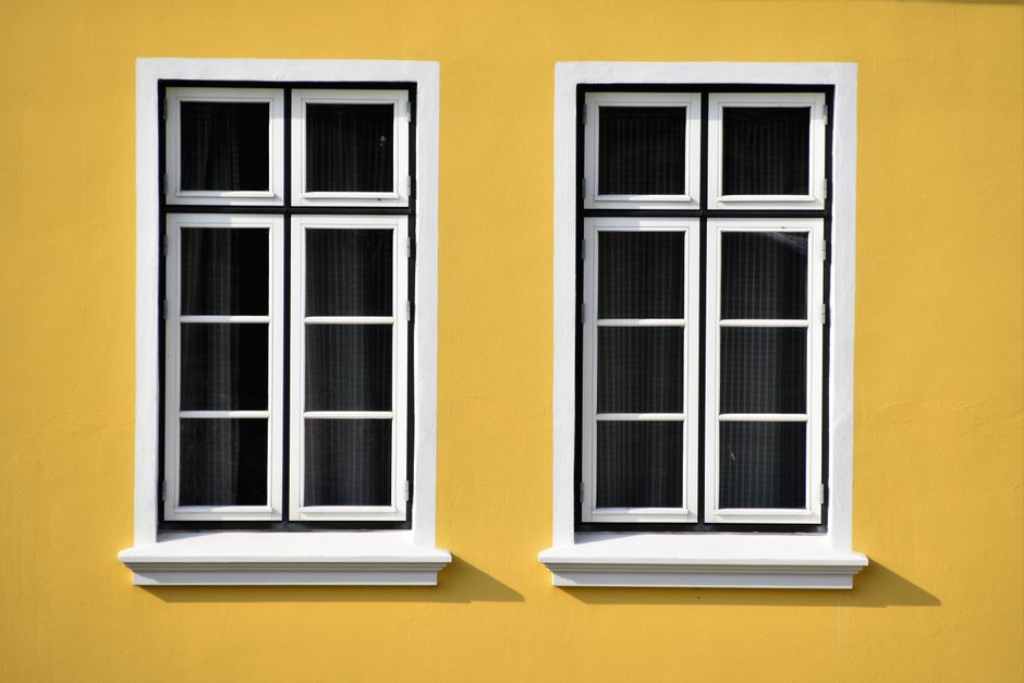 Two white-framed windows on a yellow house wall.