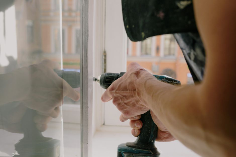 A worker fitting a white window frame with a cordless drill